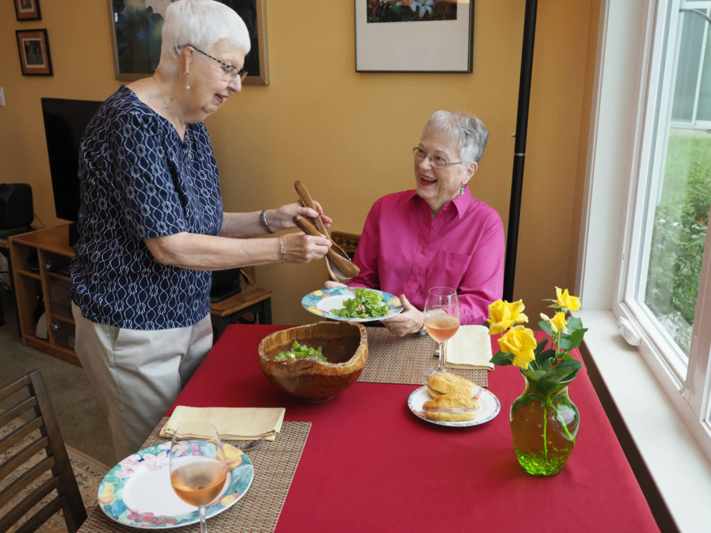 woman platting salad for another woman smiling 