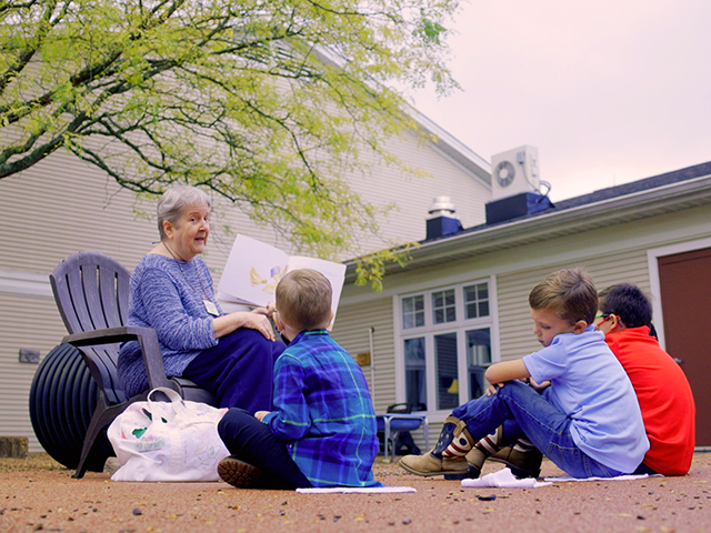 older woman reads to children outdoors