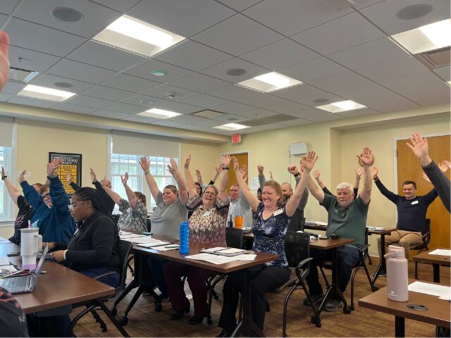 group of people doing a chair exercise with arms extended in the air