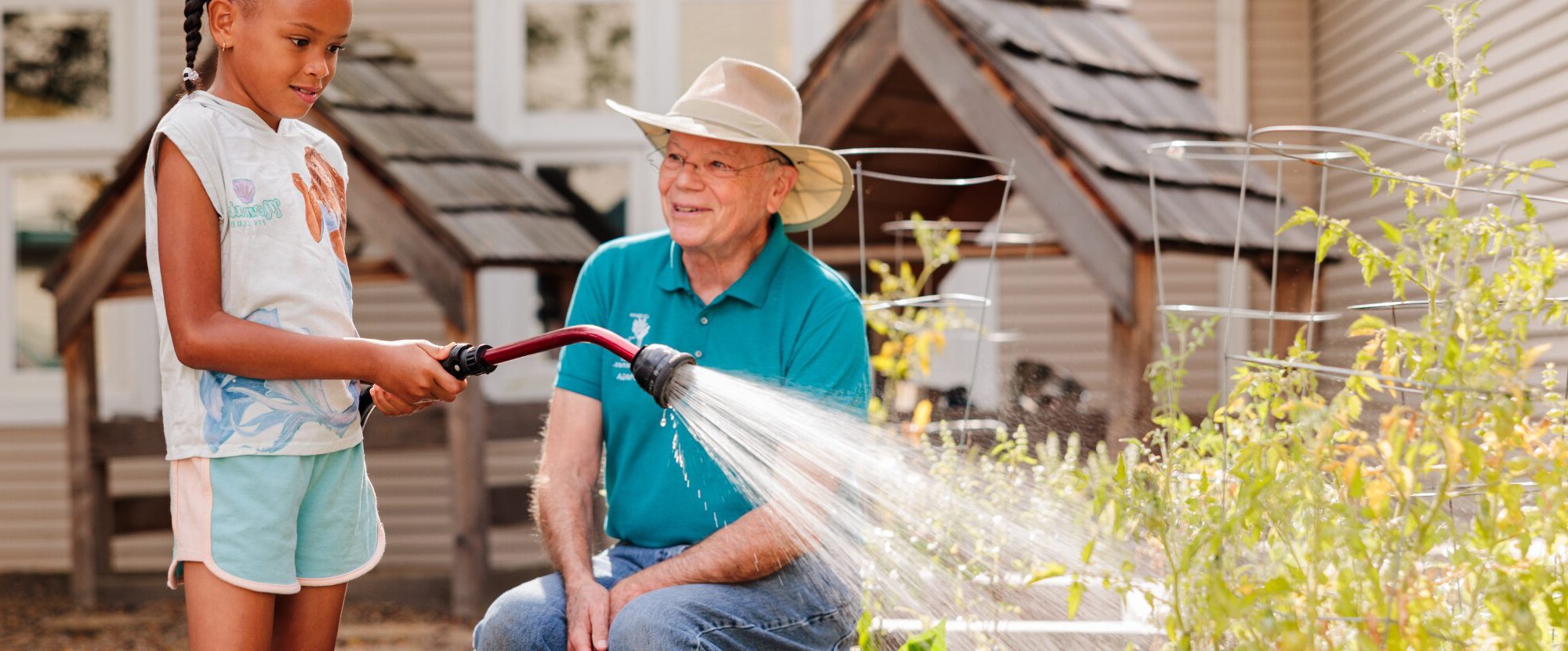 child and older man watering garden bed