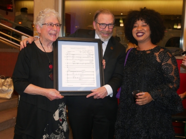 Arlene and Larry Dunn holding plaque standing next to Courtney Bryan